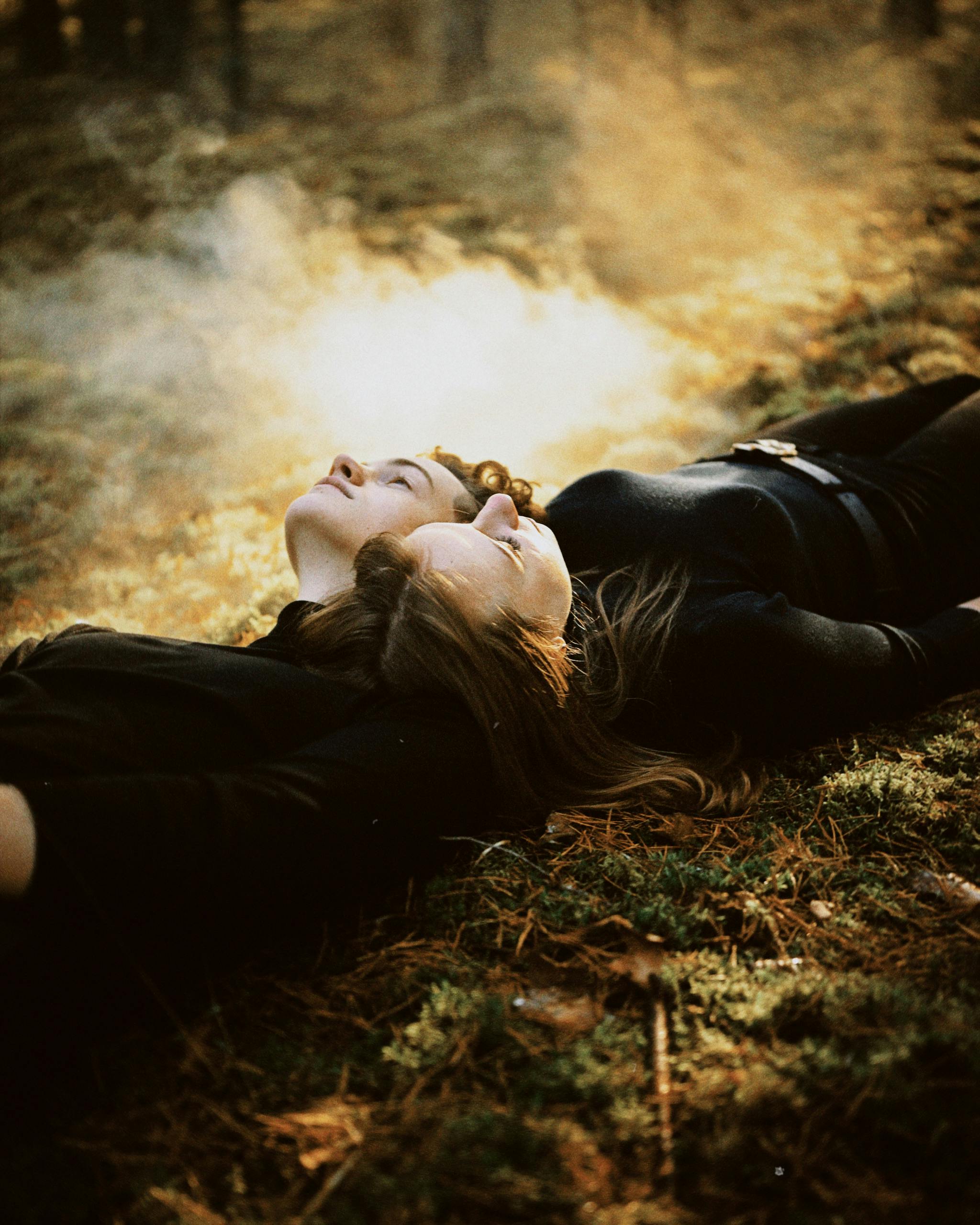 Two friends laying in a serene forest during autumn, surrounded by golden light and fog.